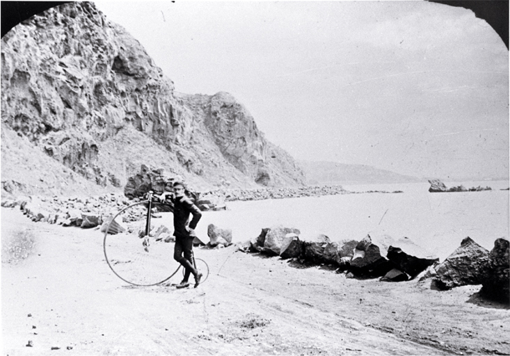 Cyclist beside a penny-farthing bicycle near Shag Rock on the Sumner road, Christchurch 