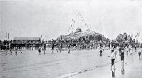 Children paddling near the pier at Cave Rock, Sumner beach, decorated for a summer carnival, Christchurch [1906]