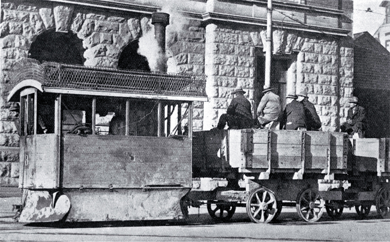 A Kitson steam tram runs past the Government Buildings in Cathedral Square with tramways workers on board 