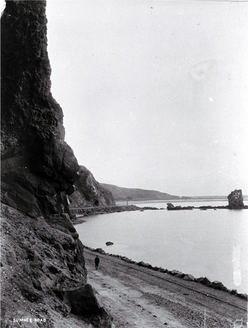 A boy stands by the tram lines along the Sumner road past the Clifton Spur and Shag Rock, Christchurch 