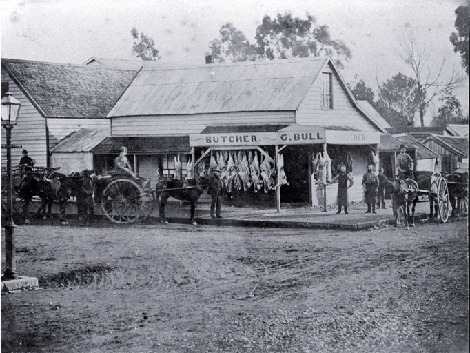 Meat hangs outside G. Bull's butchery in Cashel Street, Christchurch, with delivery carts waiting 