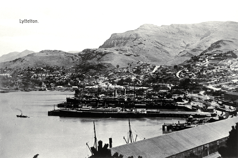 Lyttelton Harbour with ships at dock and tugboat on the water [191-?]