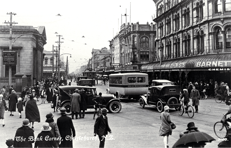 Cars, bicycles and a bus create a busy scene at the Bank corner, Christchurch : Barnett & Co. Chemists in the foreground.