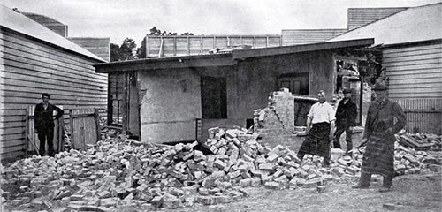 Men standing in rubble at the back of butcher/baker shop.