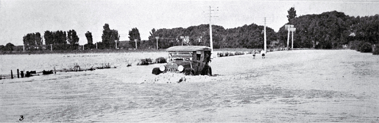 The Waimakariri river breaks its banks again over the main road : a service car negotiates the flooded road.