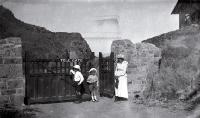 A woman with children stands outside the toll-gate to the Summit Road leading past the Sign of the Kiwi, Port Hills, Christchurch 