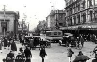 Cars, bicycles and a bus create a busy scene at the Bank corner, Christchurch : Barnett & Co. Chemists in the foreground.
